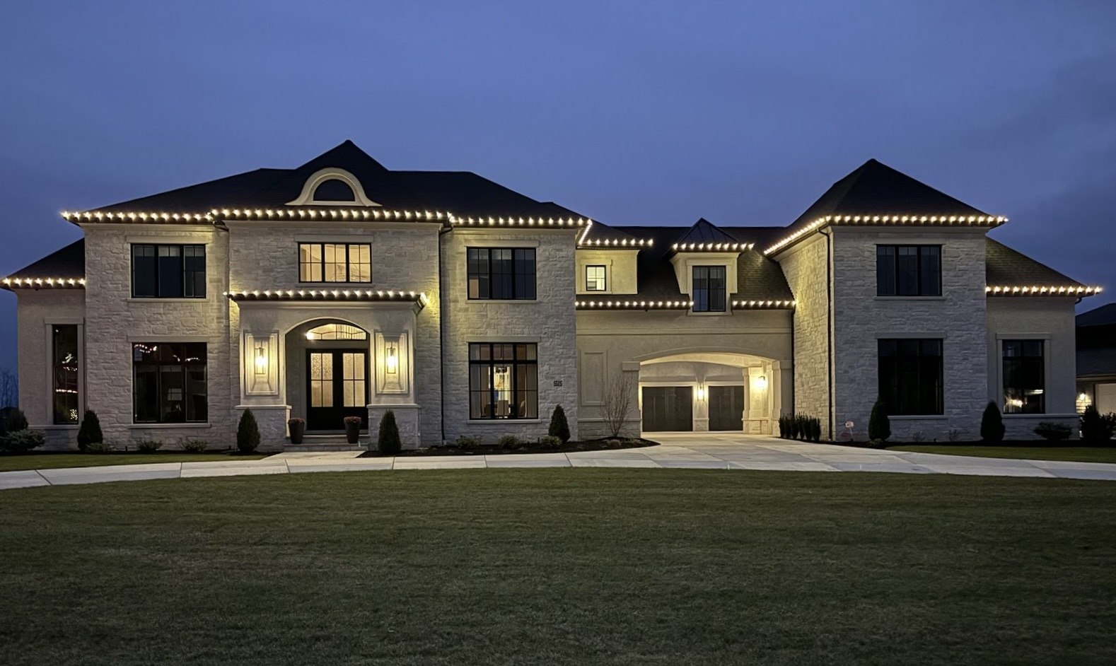 Warm white holiday lights outlining a home's roofline at dusk