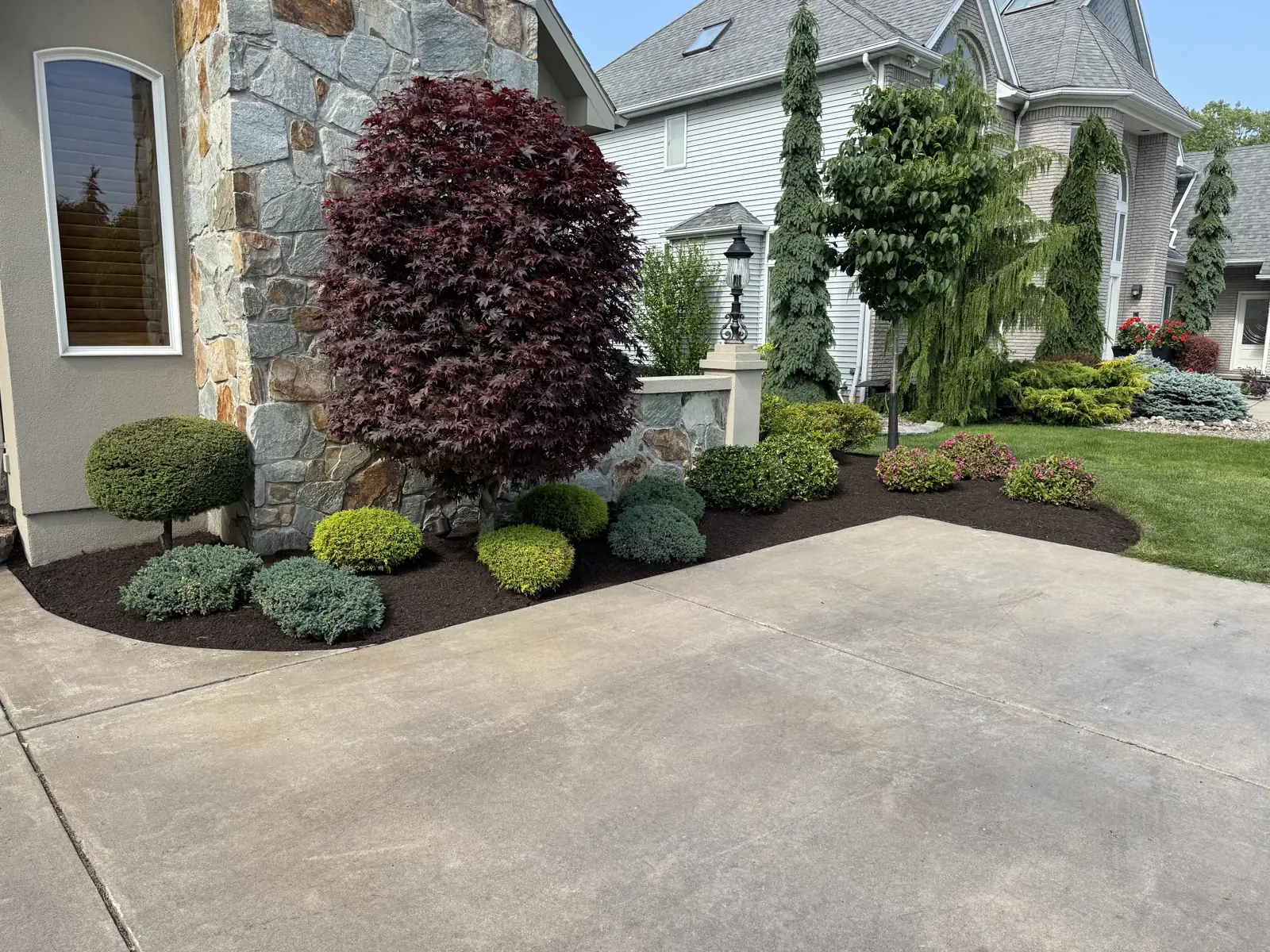 Layered ornamental plants and freshly defined mulch beds beside a stone-front home
