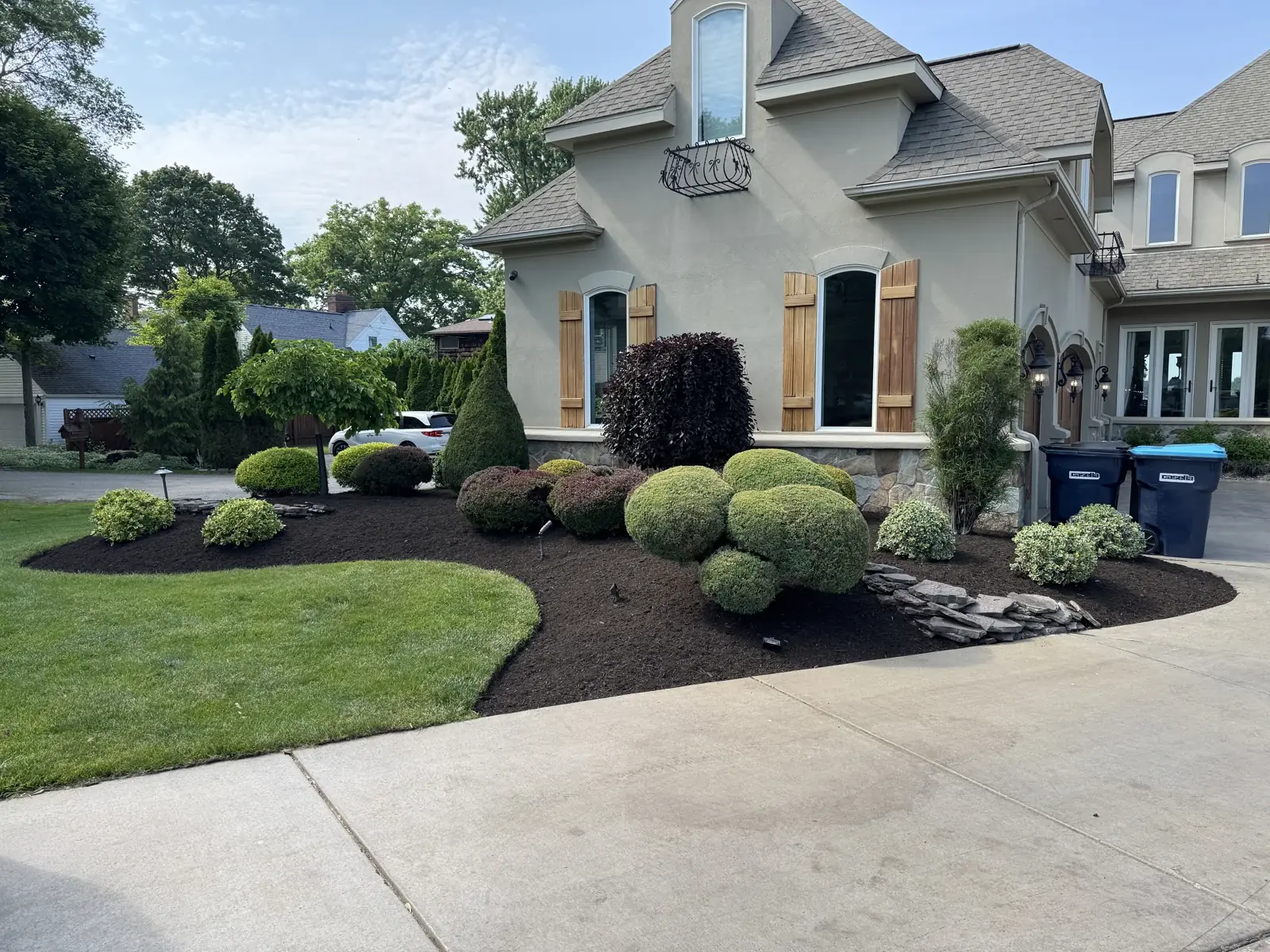 Curved mulch beds and shaped shrubs bordering a lawn and driveway