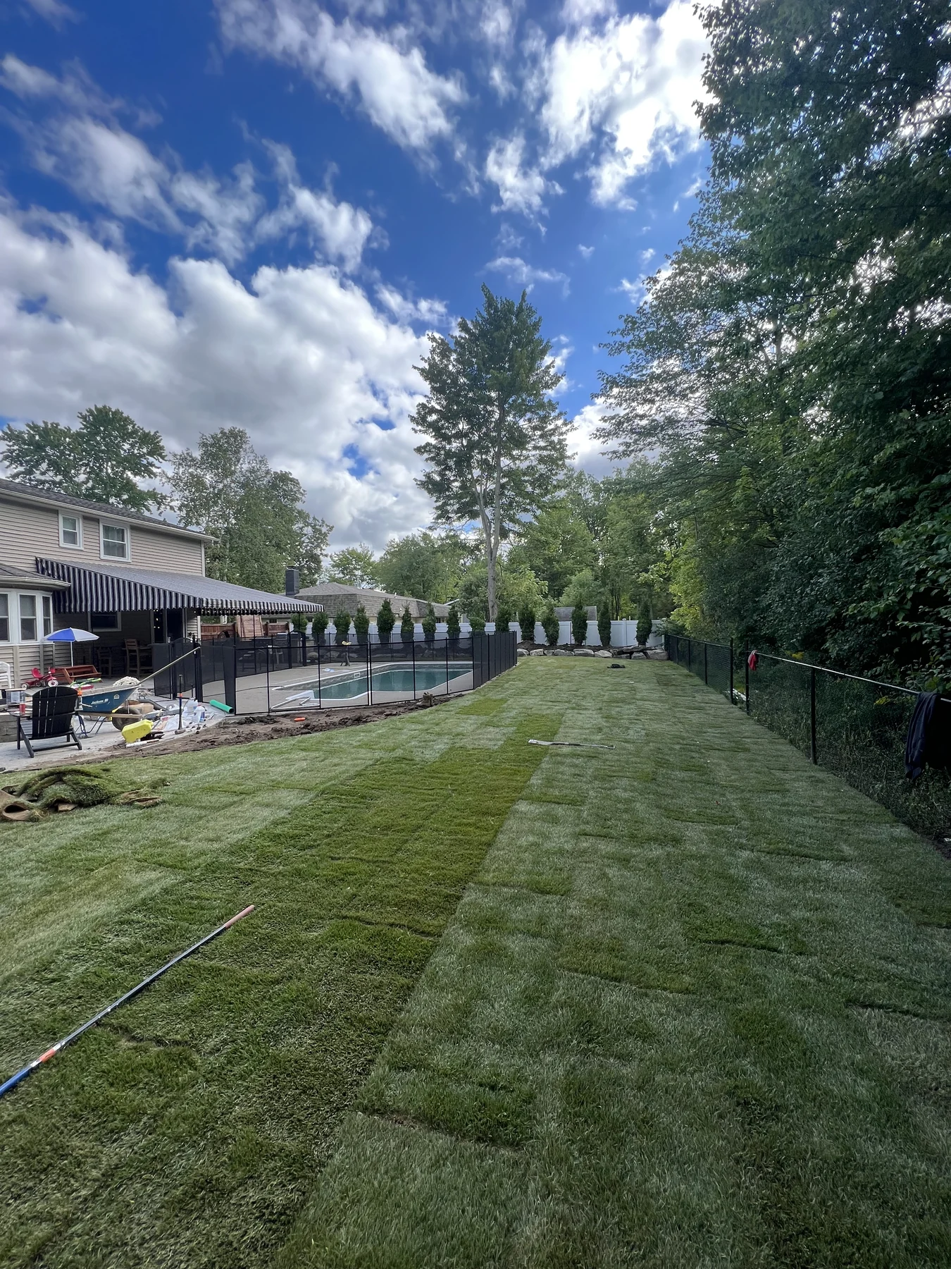 Fresh sod laid beside a pool, with visible seams and nearby landscape work still in progress